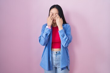 Young asian woman standing over pink background rubbing eyes for fatigue and headache, sleepy and...