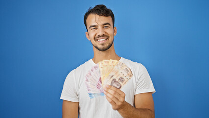 Young hispanic man smiling confident holding mexican pesos over isolated blue background - obrazy, fototapety, plakaty