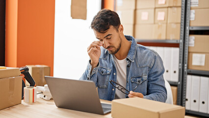 Young hispanic man ecommerce business worker stressed taking off glasses at office