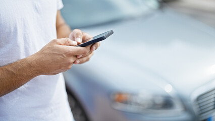 Young hispanic man using smartphone standing by car at street