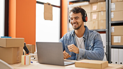 Young hispanic man ecommerce business worker listening to music dancing at office