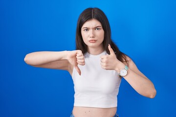 Fototapeta na wymiar Young caucasian woman standing over blue background doing thumbs up and down, disagreement and agreement expression. crazy conflict