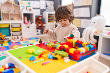 Adorable hispanic boy playing with construction blocks standing at kindergarten