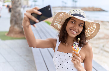 Young african american woman tourist make selfie by smartphone eating ice cream at seaside