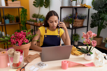 Young african american woman florist talking on smartphone using laptop at flower shop