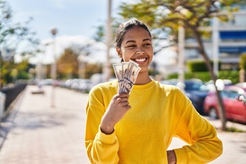 Young african american woman smiling confident holding dollars at street