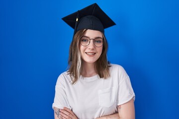 Blonde caucasian woman wearing graduation cap happy face smiling with crossed arms looking at the camera. positive person.