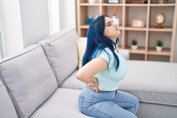 Young caucasian woman suffering for backache sitting on sofa at home
