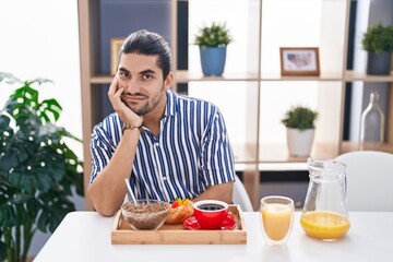 Fototapeta na wymiar Hispanic man with long hair sitting on the table having breakfast thinking looking tired and bored with depression problems with crossed arms.