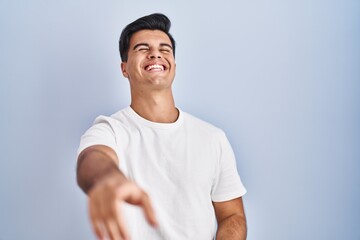 Fototapeta premium Hispanic man standing over blue background laughing at you, pointing finger to the camera with hand over body, shame expression