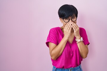 Young asian woman with short hair standing over pink background laughing and embarrassed giggle...