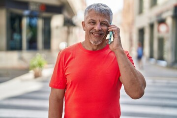 Middle age grey-haired man smiling confident talking on the smartphone at street