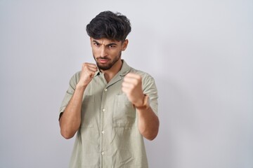 Arab man with beard standing over white background ready to fight with fist defense gesture, angry and upset face, afraid of problem