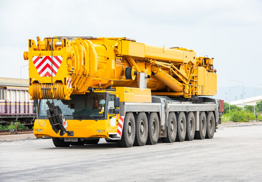 Mobile cranes 500 ton construction cranes with yellow telescopic arms and big tower cranes in sunny day with white clouds and deep blue sky on background, heavy industry port