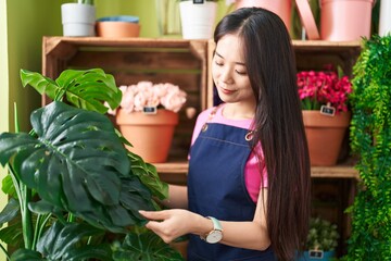 Young chinese woman florist smiling confident touching plant at flower shop