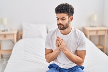 Young arab man praying sitting on bed at bedroom