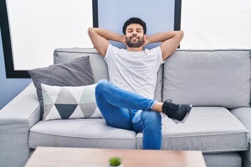 Young arab man relaxed with hands on head sitting on sofa at home