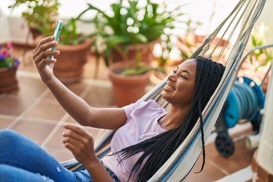African american woman make selfie by smartphone lying on hammock at home terrace