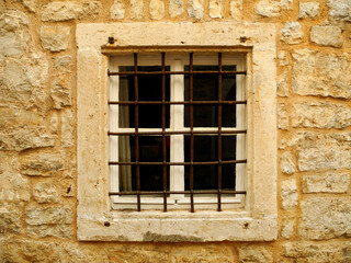 Old window with white wooden frame and iron bars in yellow stone wall 
