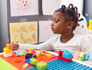 African american girl playing with construction blocks sitting on table at kindergarten