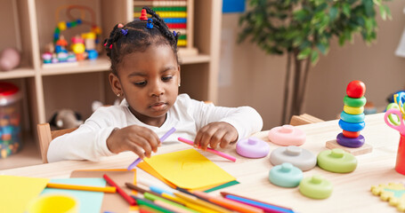 African american girl preschool student sitting on table drawing on paper at kindergarten