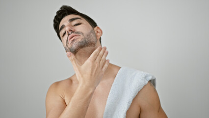 Young hispanic man standing shirtless applying beard treatment over isolated white background