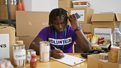 African american man volunteer listening to voice message writing on document at charity center