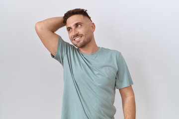 Hispanic man with beard standing over white background smiling confident touching hair with hand up gesture, posing attractive and fashionable