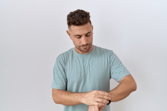 Hispanic man with beard standing over white background checking the time on wrist watch, relaxed and confident