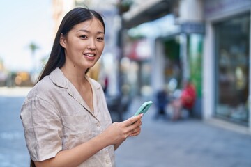 Chinese woman smiling confident using smartphone at street