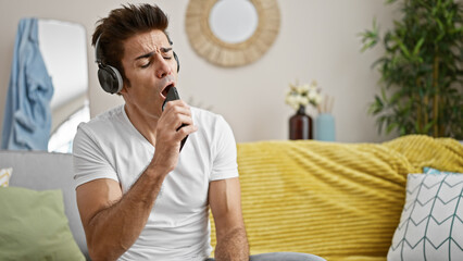 Young hispanic man singing song using smartphone as a microphone at home