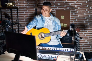 Hispanic young man playing classic guitar at music studio smiling friendly offering handshake as greeting and welcoming. successful business.