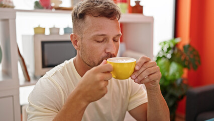 Fototapeta na wymiar Young man smelling cup of coffee sitting on table at dinning room