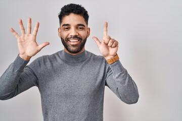 Fototapeta premium Hispanic man with beard standing over white background showing and pointing up with fingers number seven while smiling confident and happy.