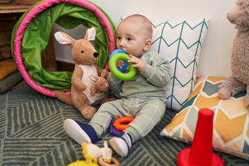 Adorable caucasian baby sitting on floor sucking hoops at home