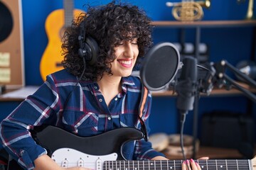 Young middle east woman artist singing song playing electrical guitar at music studio