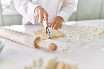 Fototapeta na wymiar Young woman wearing cook uniform cutting pasta dough at kitchen