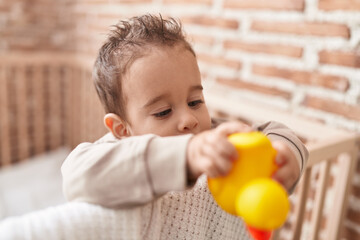 Adorable hispanic boy holding duck toy standing on cradle at bedroom