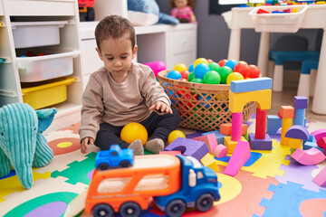 Adorable hispanic boy playing with balls sitting on floor at kindergarten