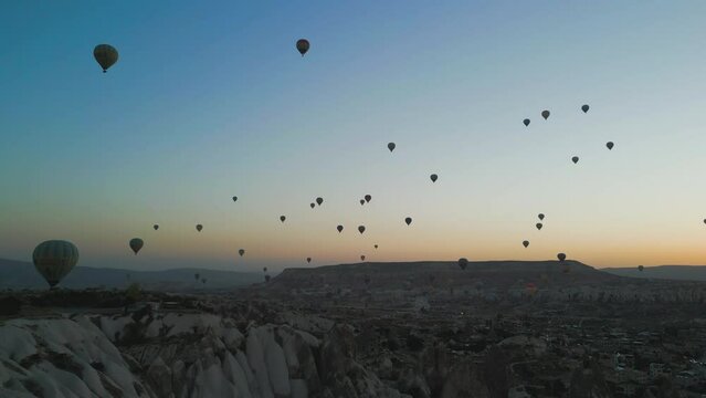 Drone view of air balloons flying above rough mountain landscapes during sunset
