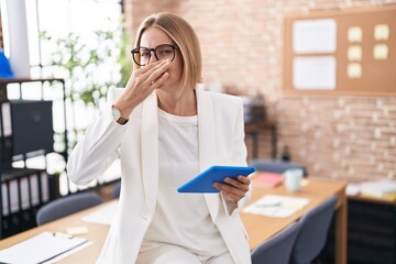 Young caucasian woman working at the office wearing glasses smelling something stinky and...