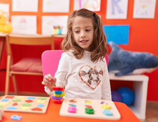 Adorable hispanic girl playing with maths puzzle game sitting on table at kindergarten