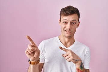 Caucasian man standing over pink background pointing aside worried and nervous with both hands,...