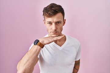 Caucasian man standing over pink background cutting throat with hand as knife, threaten aggression...