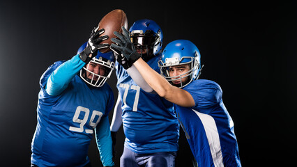 Three American football players raising their hands up holding the ball on a black background. 