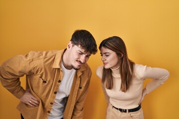 Young hispanic couple standing over yellow background suffering of backache, touching back with hand, muscular pain