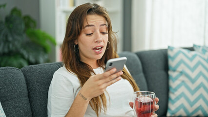 Young beautiful hispanic woman drinking tea sending voice message by smartphone at home