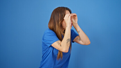 Young beautiful hispanic woman doing binoculars gesture with hands looking for over isolated blue...