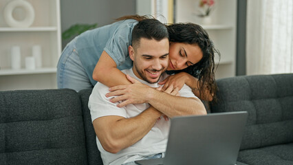 Man and woman couple using laptop hugging each other at home