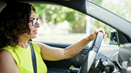 Fototapeta na wymiar Middle age hispanic woman driving a car smiling wearing glasses on the road